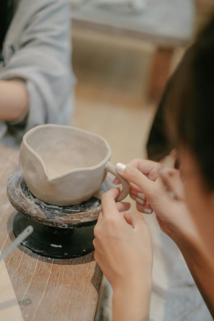 Close-up of hands molding a clay pitcher on a pottery wheel, showcasing craftsmanship.